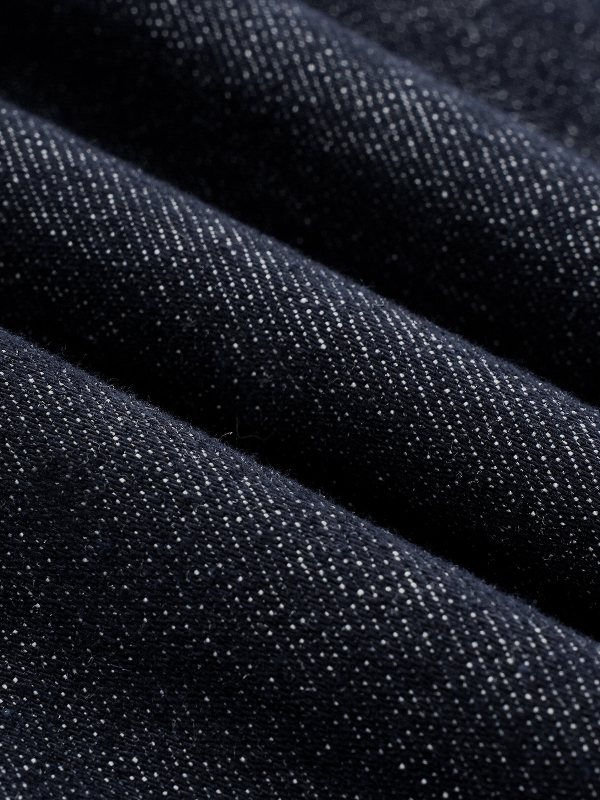 Close-up of dark indigo denim fabric with a visible twill weave texture, arranged in soft diagonal folds.
