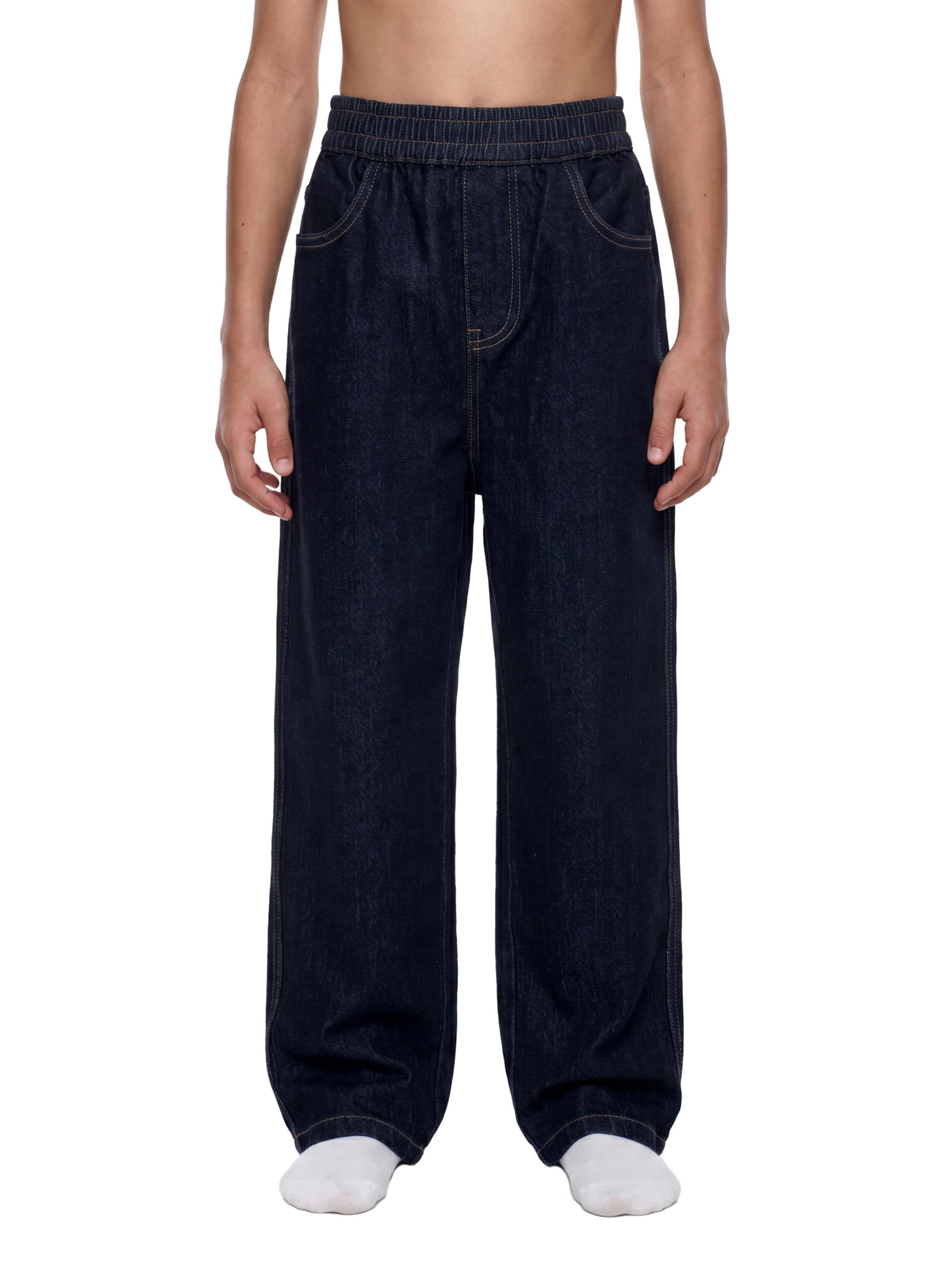 A person wearing very loose dark indigo denim pants with an elastic waistband, shown from the waist down against a plain white background.