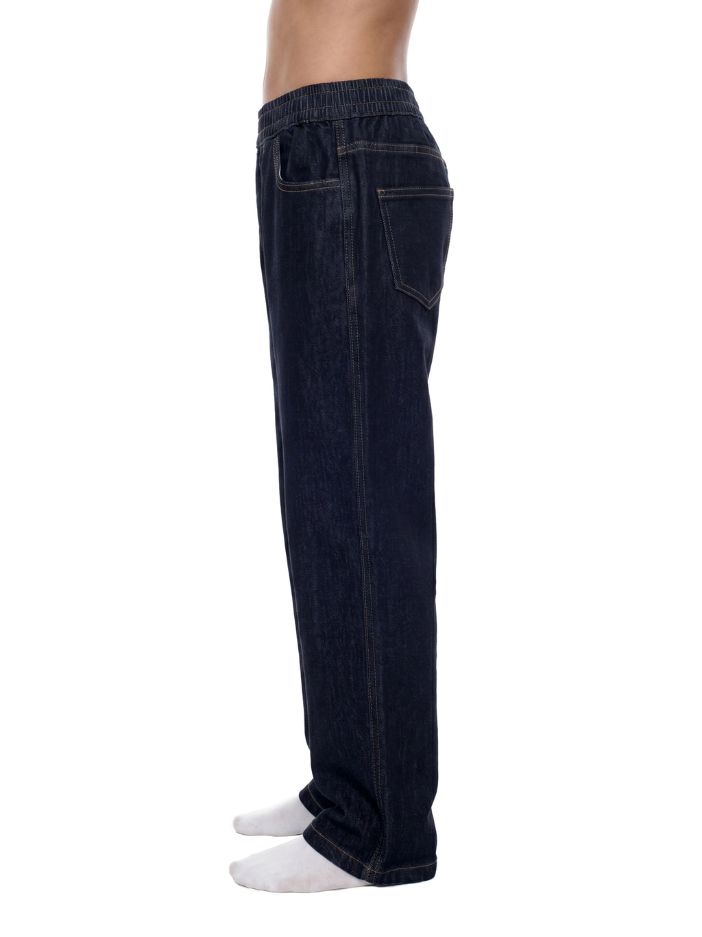Side view of a person wearing dark indigo denim jogger pants with white socks, shown against a plain white background.