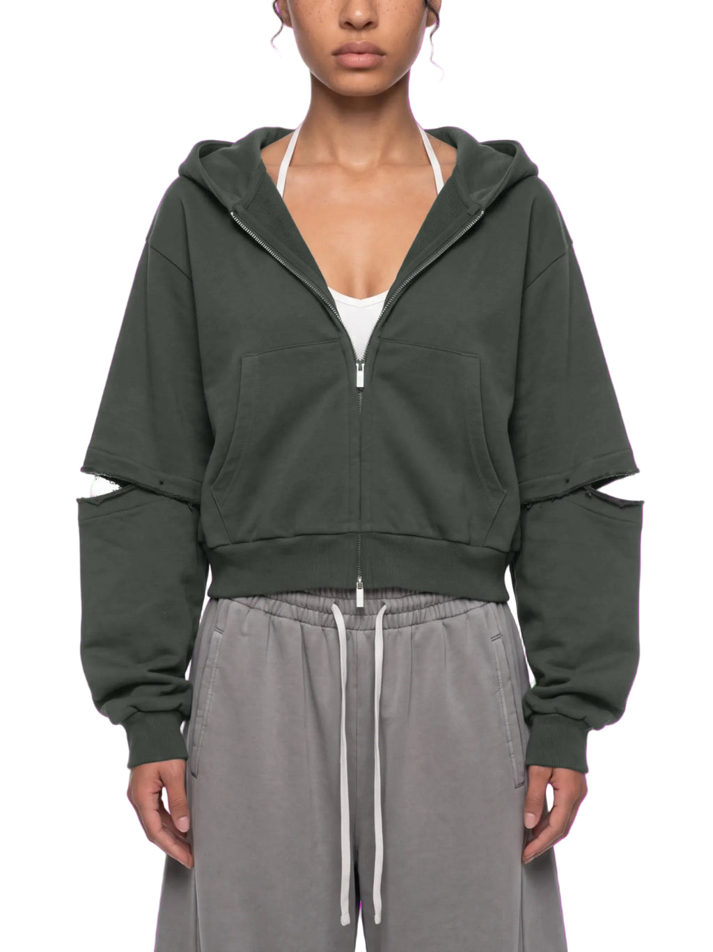 A model wearing a dark olive green cropped zip-up hoodie with distressed details on the sleeves, styled with gray drawstring sweatpants against a white background.