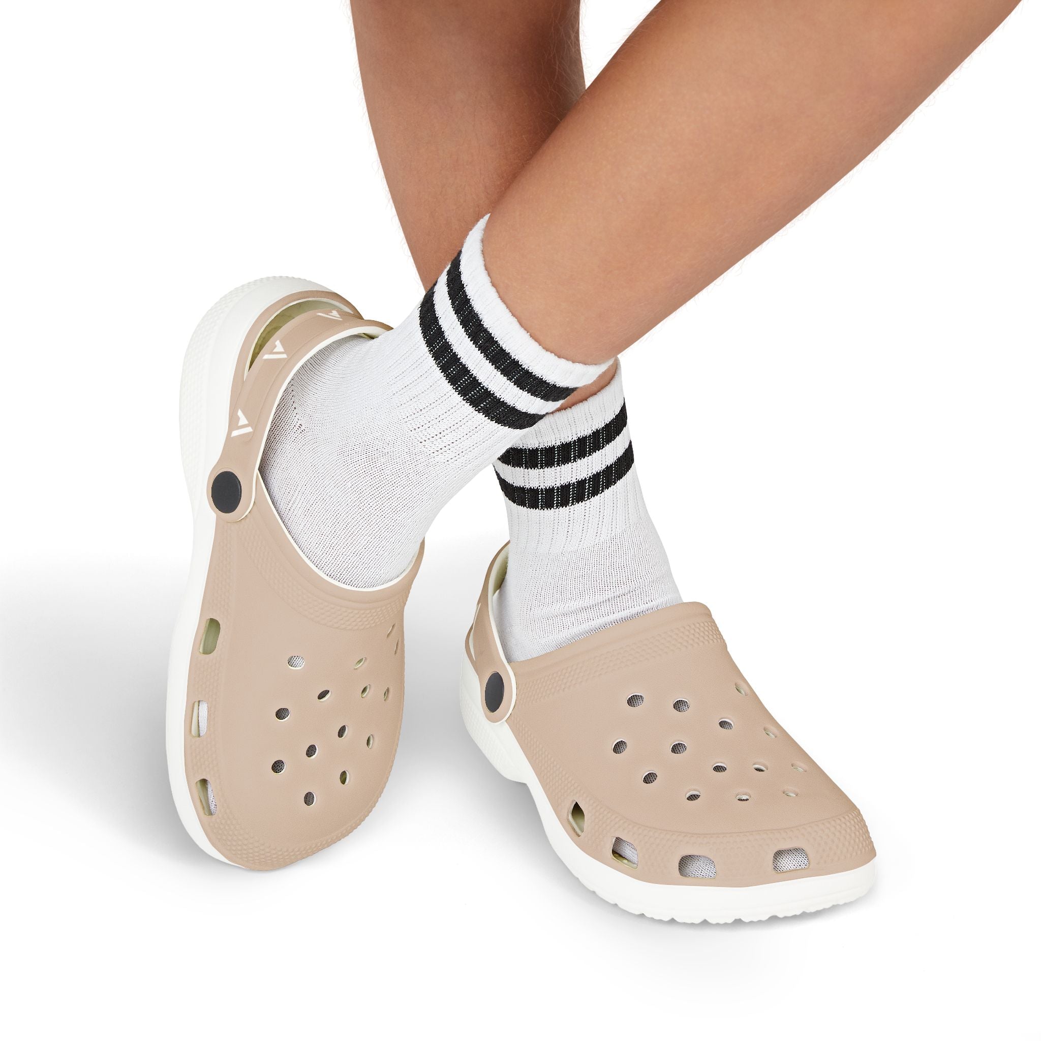 Beige foam clogs with white soles worn with white crew socks featuring black stripes, shown on a person's feet against a white background.