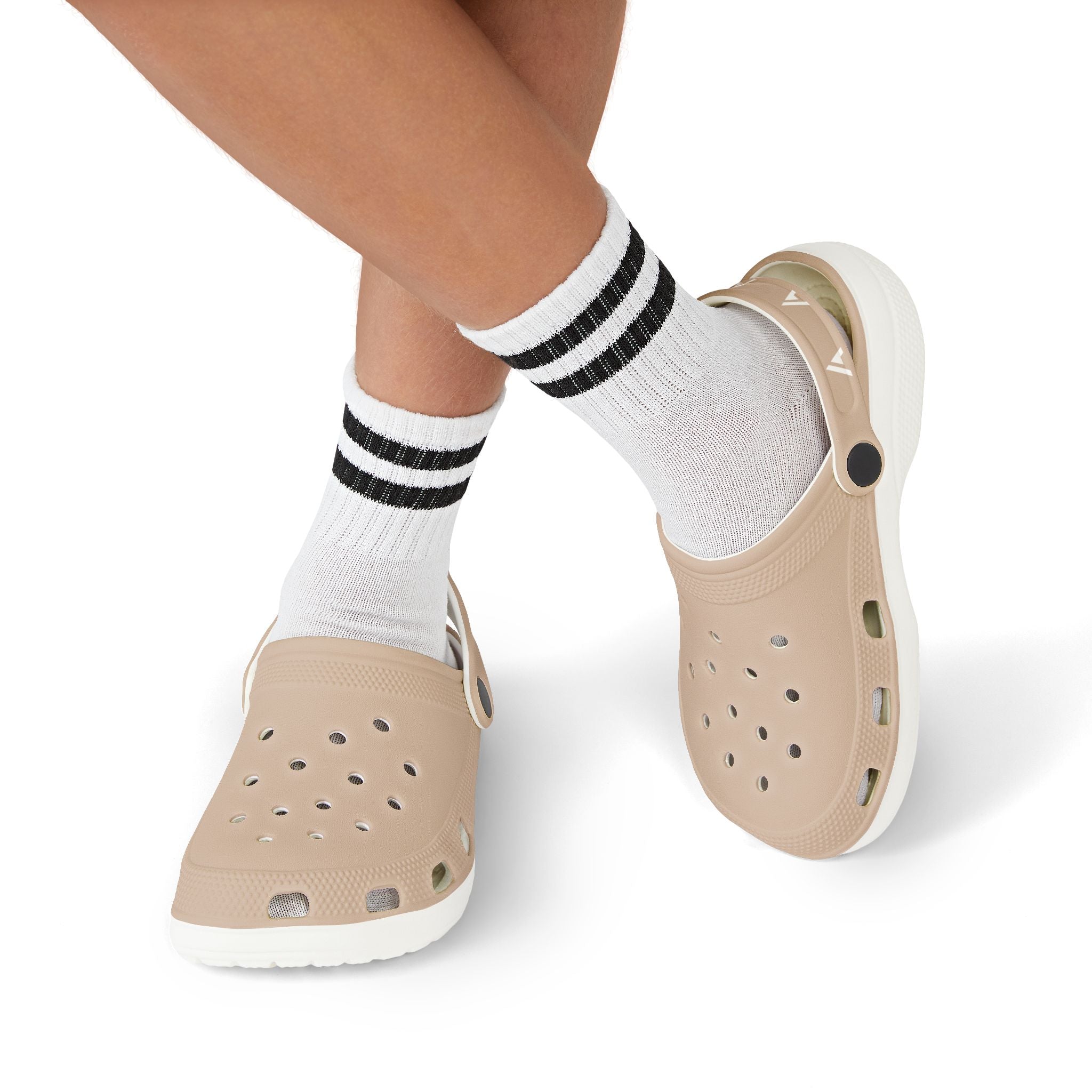 Beige slip-on clogs with white soles worn with white crew socks featuring black stripes, shown on a person's feet against a white background.