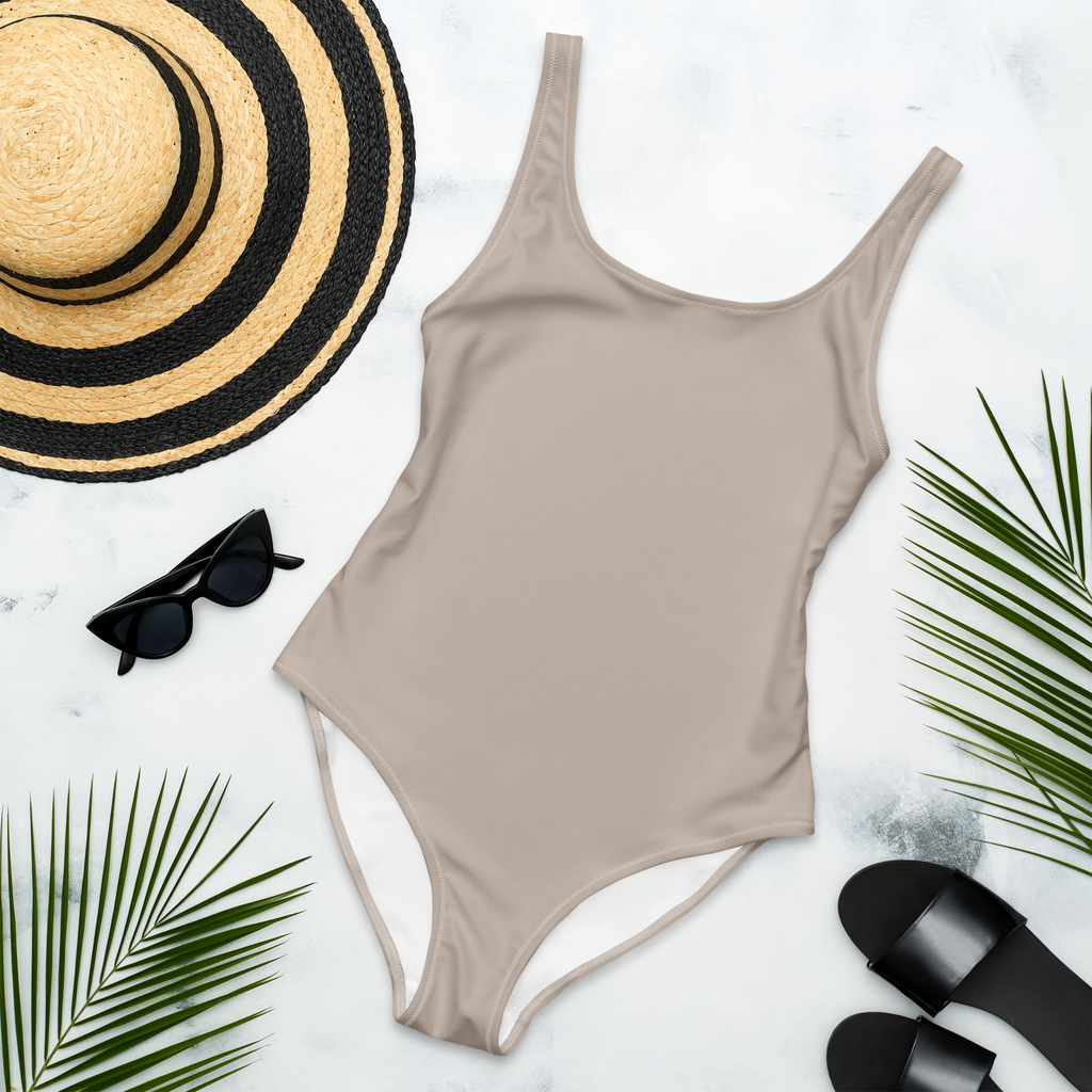 Beige swimsuit with black sunglasses, straw hat, and black sandals on a light background